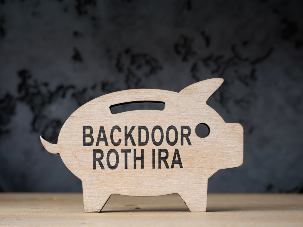 Wooden piggy-bank cut-out that reads “Backdoor Roth IRA” on a dark background