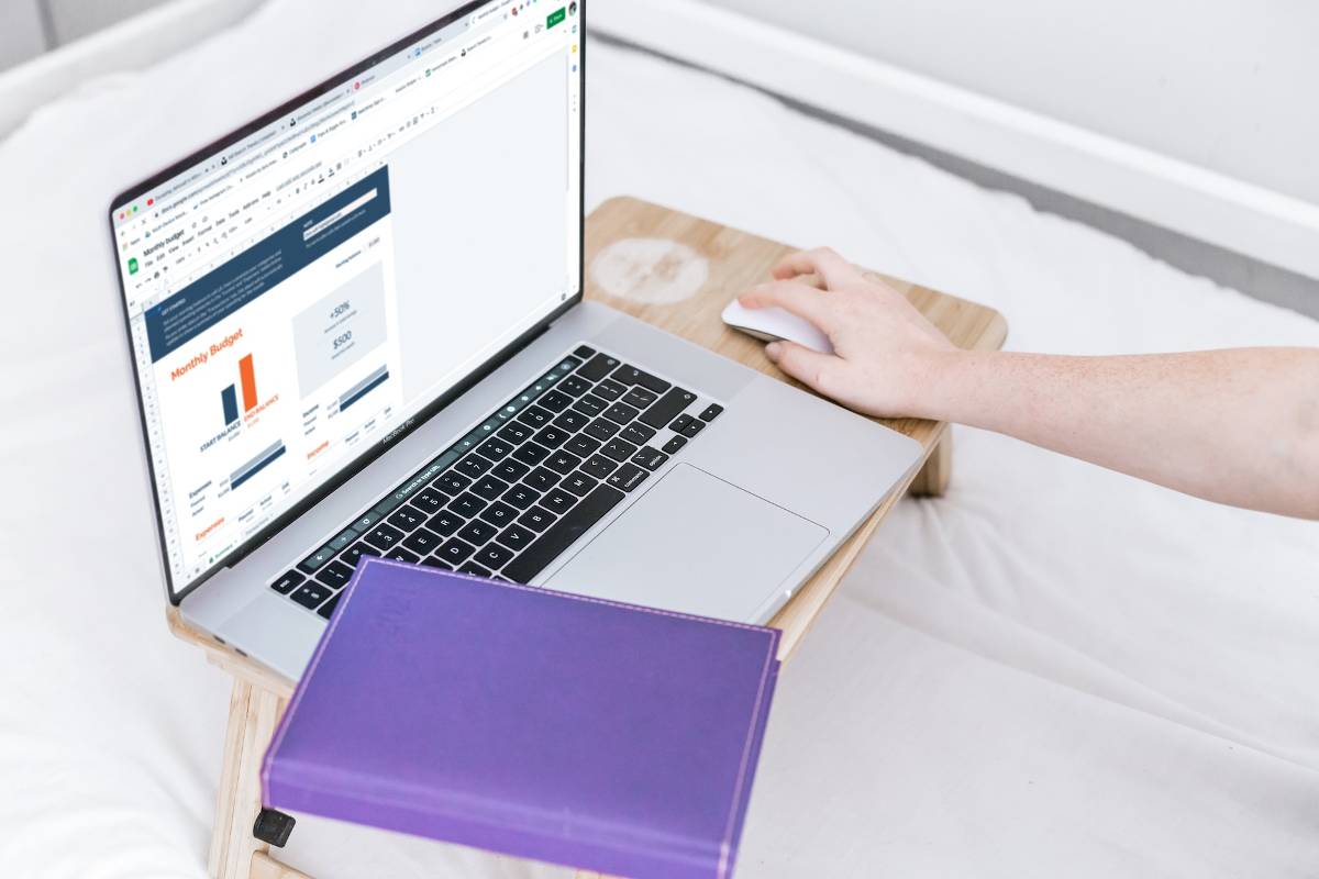Person working on a budget spreadsheet on a laptop, a purple notebook beside it