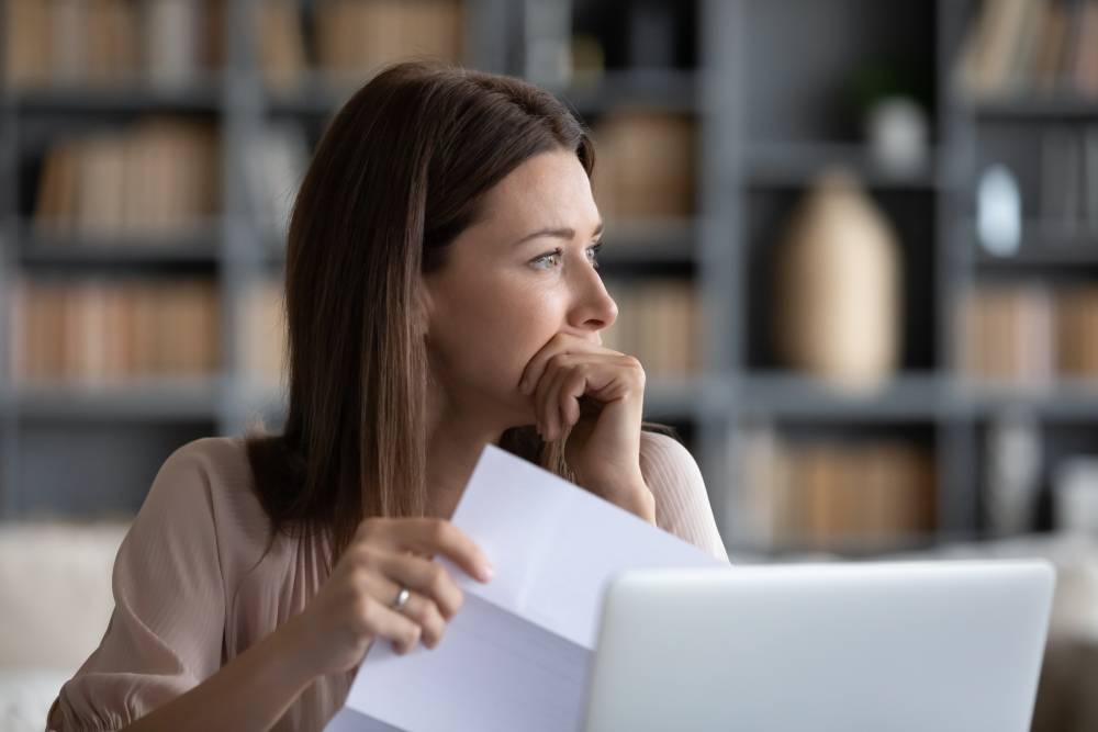Woman at a laptop looking pensively at a bill she is holding