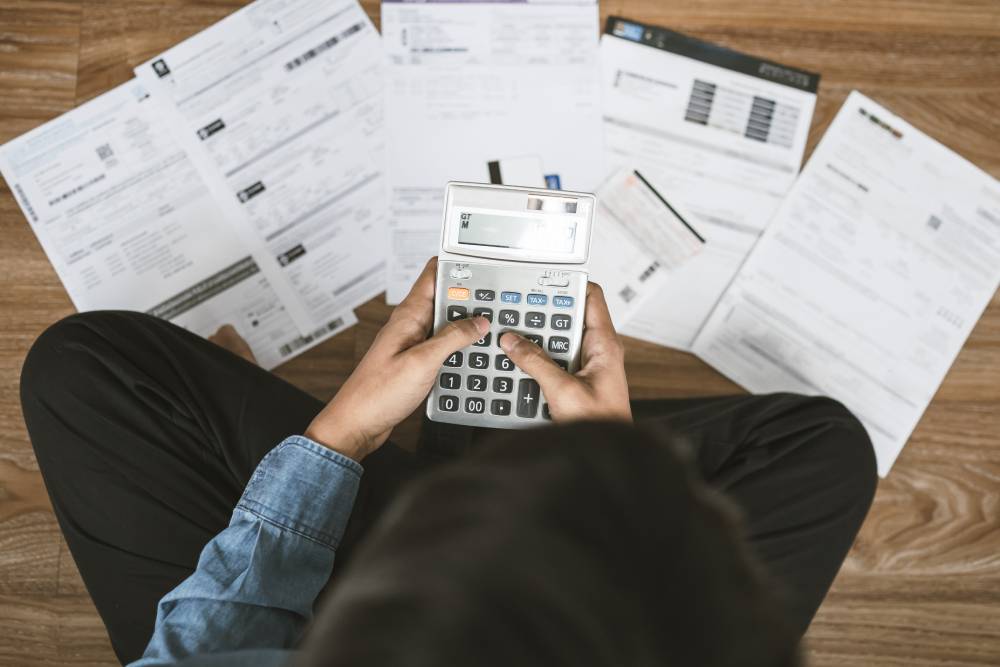 Person on the floor using a calculator amid spread-out financial statements