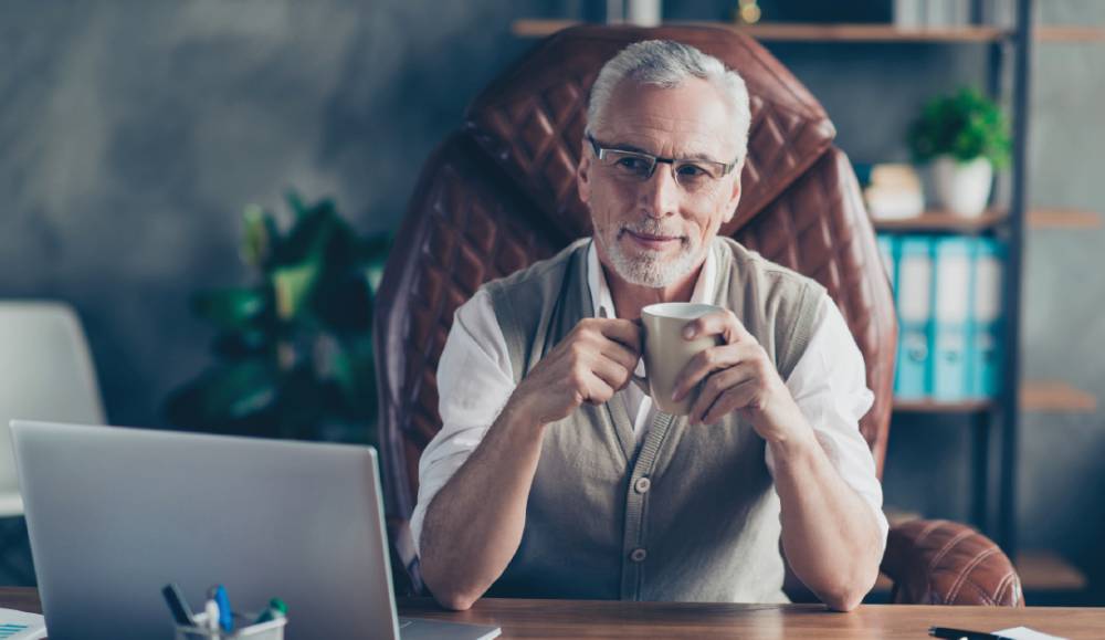Older man with a coffee cup at a desk with a laptop