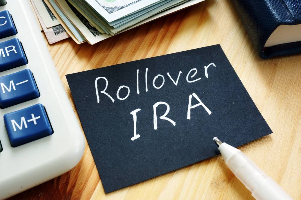 Black card reading “Rollover IRA” beside a calculator, cash and a pen