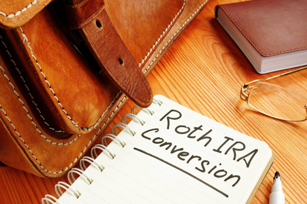 Notebook reading “Roth IRA Conversion” beside a leather bag and reading glasses