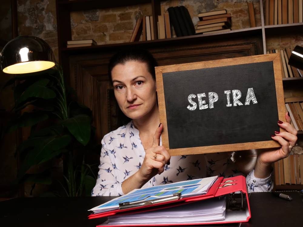 Woman at a desk holding a small chalkboard that reads “SEP IRA”