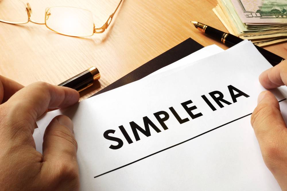 Hand holding a sheet of paper that reads “SIMPLE IRA” over a desk