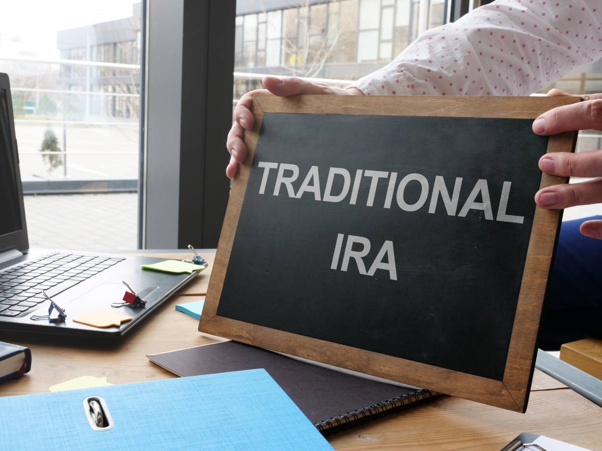 Hands holding a chalkboard that reads “Traditional IRA” above a laptop on a desk