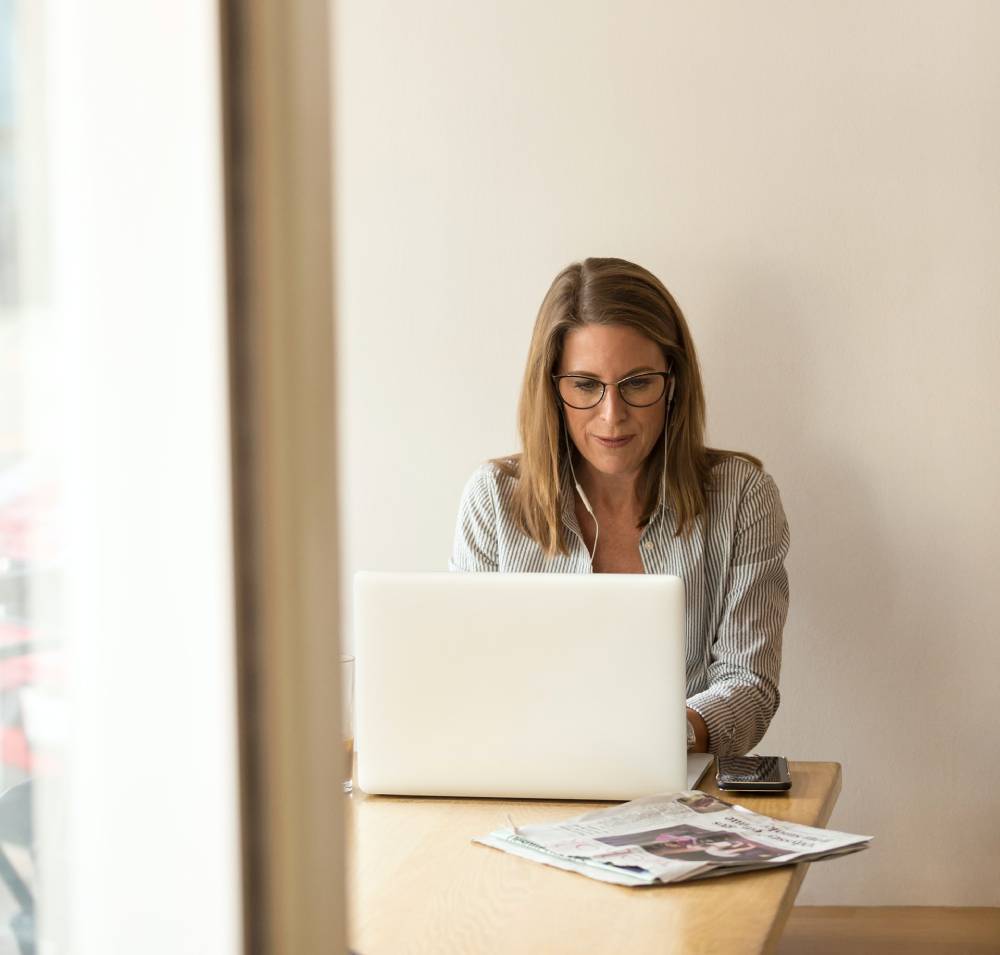 Woman with glasses working at a laptop by a sunlit window